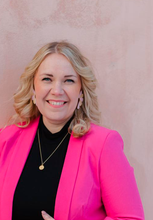 Hymyilevä Heidi Kirjaston vaaleanpunaista seinää vasten