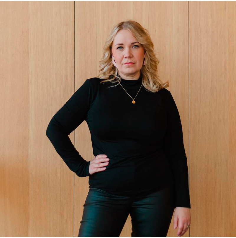 WhatsApp Image 2025-02-22 at 13.50.27 800x800 (4) Heidi Aaltonen seisoo puisen seinän edessä käsi lantiolla